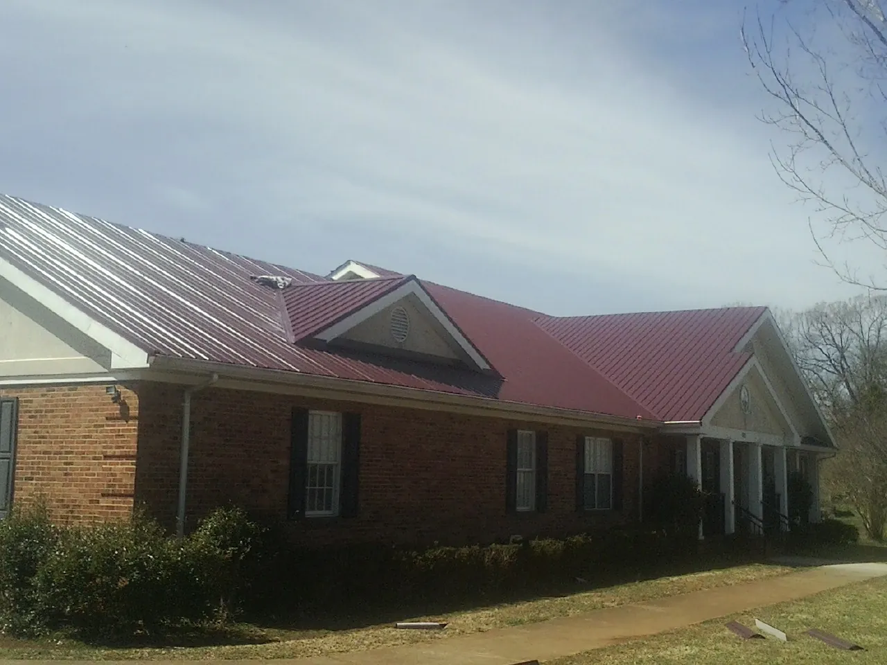 Red metal roof with gabled entries on a long brick building, from a Hail Damage Roof Repair job in New Cumberland