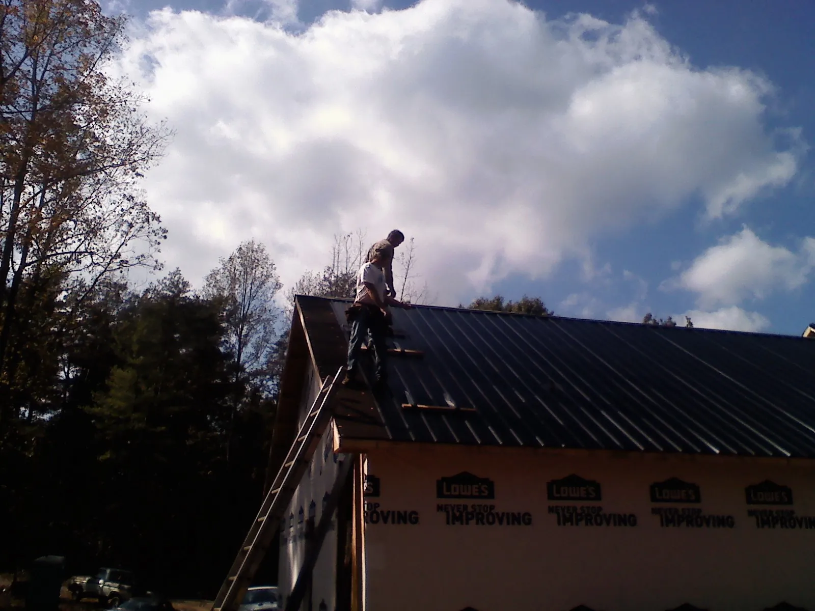 Roofer fastening dark metal panels high against a cloudy sky, from a Roof Inspection job in New Cumberland