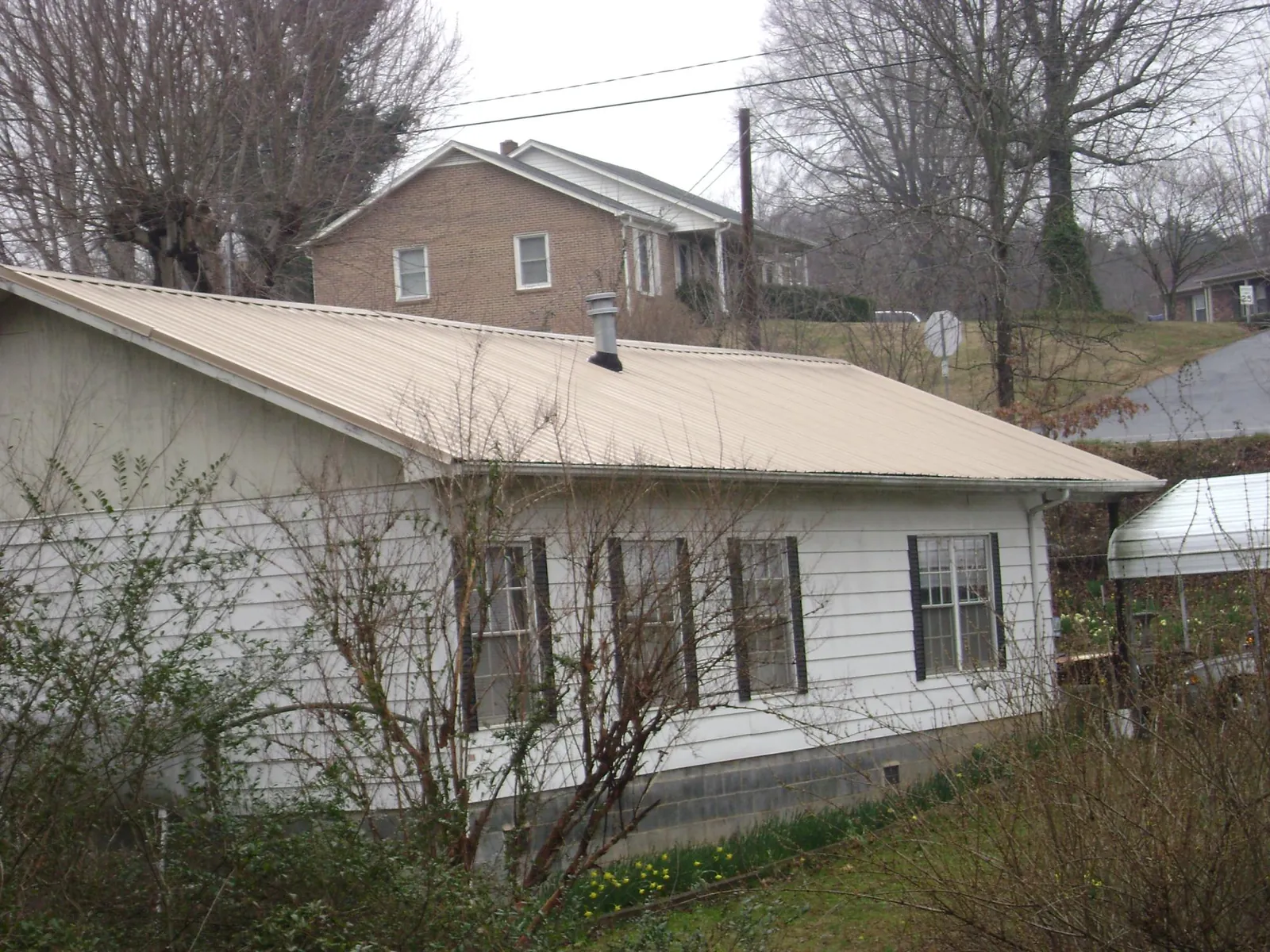 Tan metal roof on a white sided house set into a hillside — Commercial Roofing by Roofing Brothers in New Cumberland